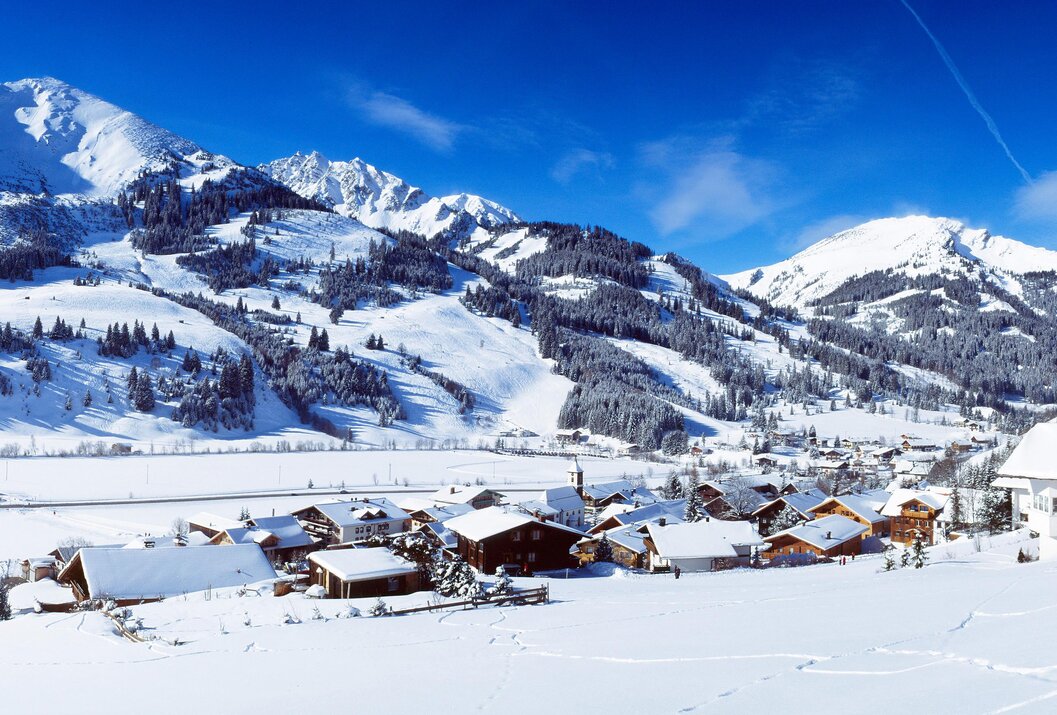 Winterliche Landschaft mit schneebedeckten Häusern und Bergen unter blauem Himmel