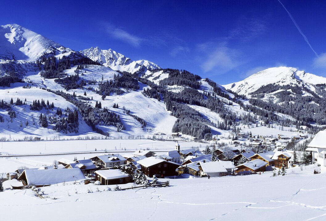 Winterliche Berglandschaft mit schneebedeckten Häusern unter blauem Himmel