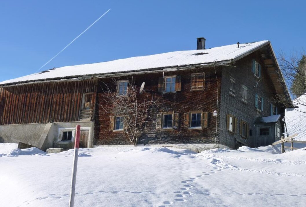 Altes Holzhaus im Schnee unter blauem Himmel mit Kondensstreifen