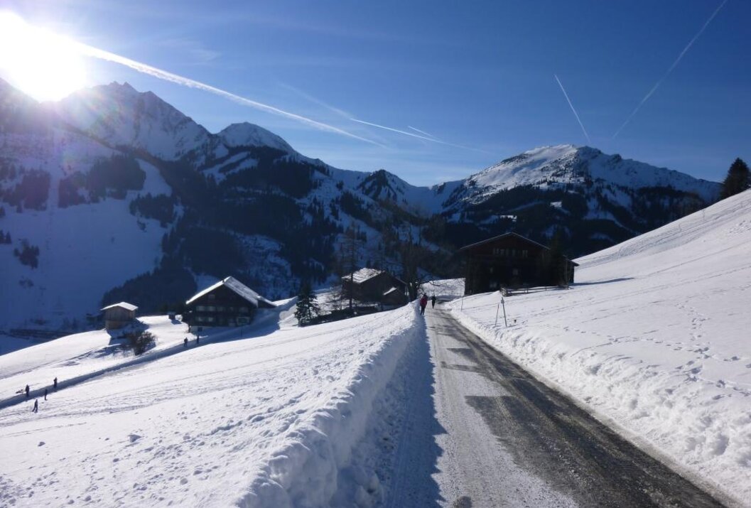 Winterlandschaft mit schneebedeckten Bergen, Häusern und einer Straße unter blauem Himmel