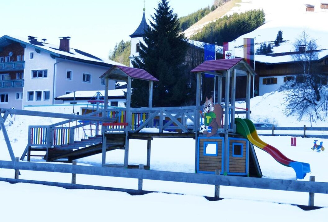 Spielplatz im Schnee vor Häusern und Kirche in Berglandschaft