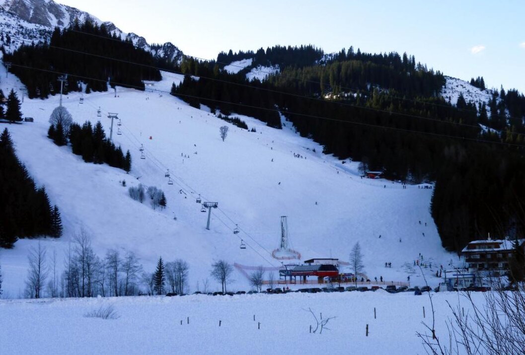 Verschneite Skipiste mit Liftanlagen vor bewaldetem Berg