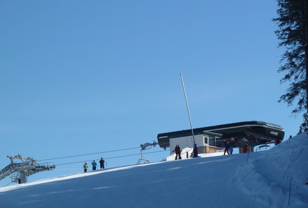 Skiliftstation auf schneebedecktem Hügel unter blauem Himmel mit einigen Personen