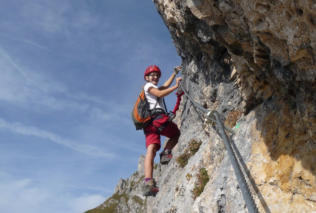 Kletterer am Felsen mit Helm und Rucksack auf einem Klettersteig