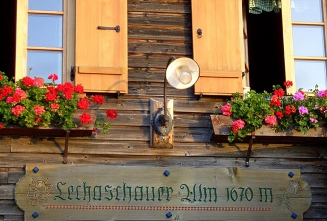 Holzhausfassade mit Fensterläden, Blumenkästen und Schild "Lechaschauer Alm 1670 m"