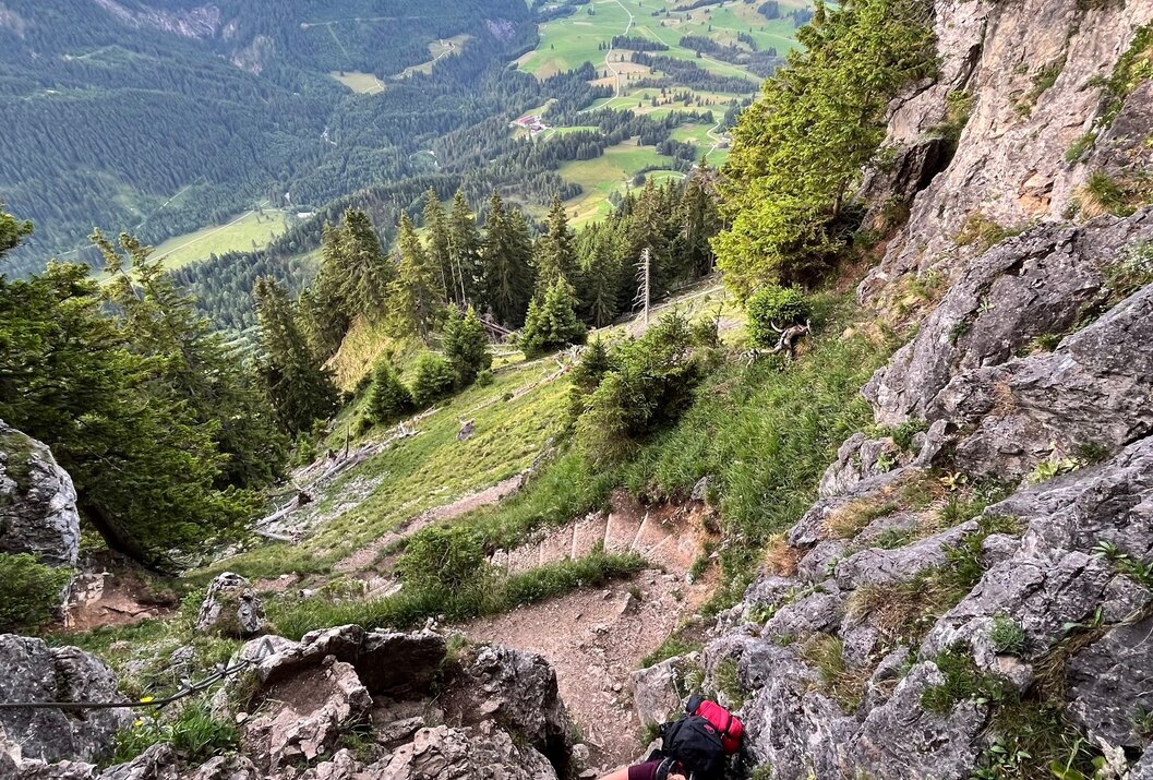 Kletterer am Felsenhang mit Blick auf bewaldetes Tal und Bergkette