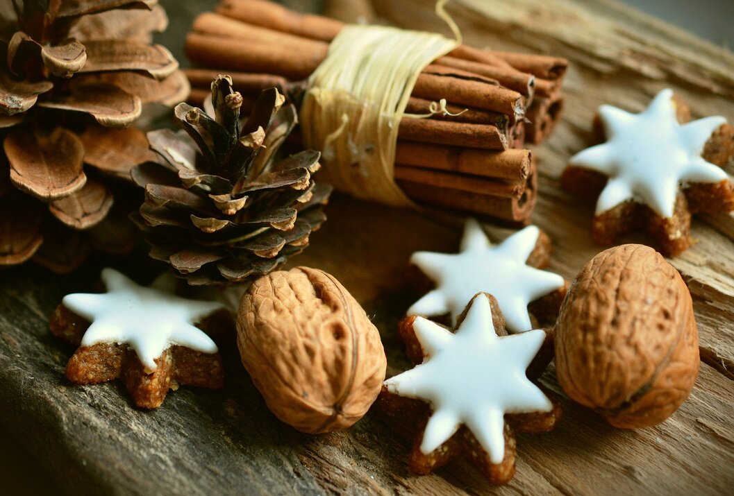 Weihnachtliche Dekoration mit Zimtstangen, Tannenzapfen, Nüssen und Sternkeksen auf Holz