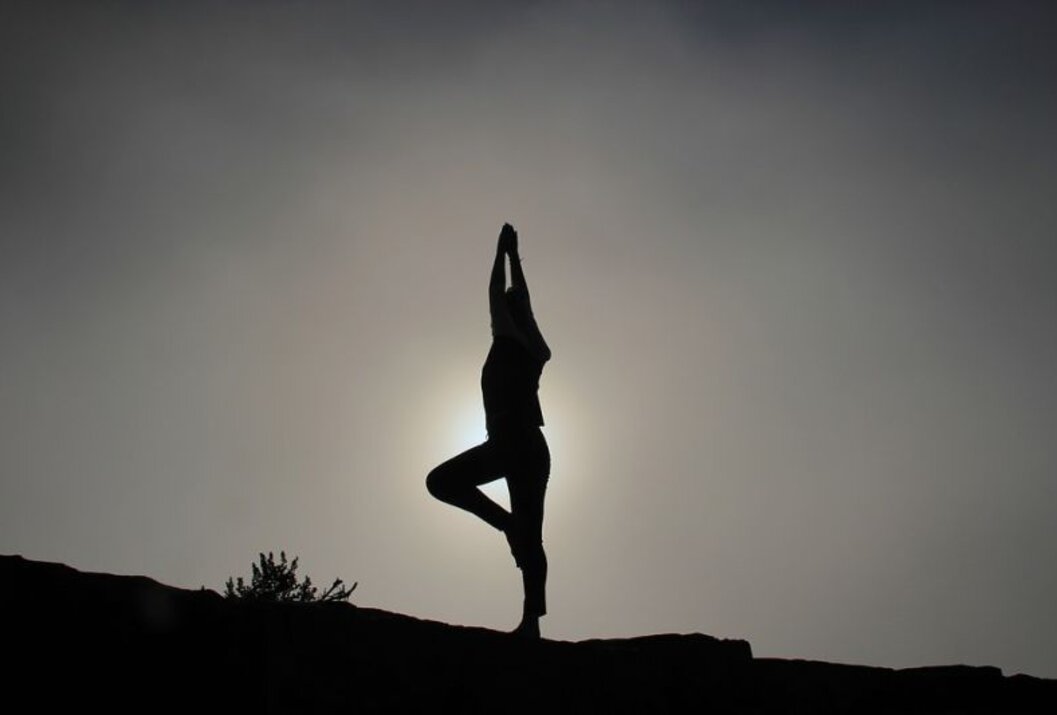 Silhouette einer Person in Yoga-Baumstellung vor hellem Hintergrund