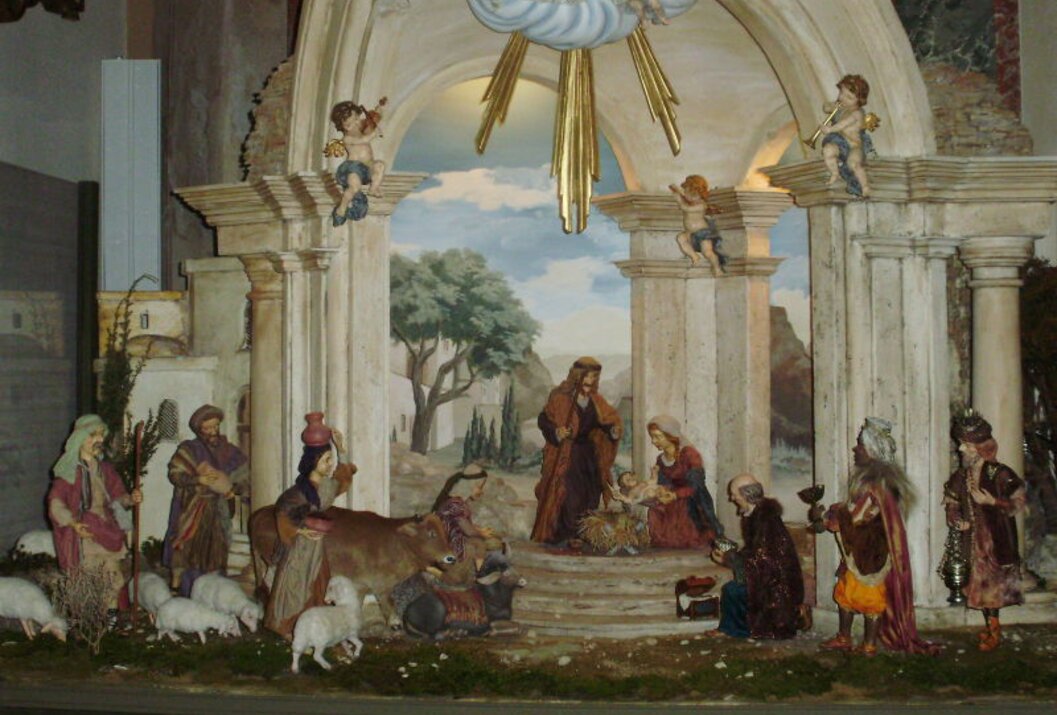 Krippendarstellung mit Maria, Josef, Jesuskind, Hirten, Tieren und Engeln vor gemalter Landschaft