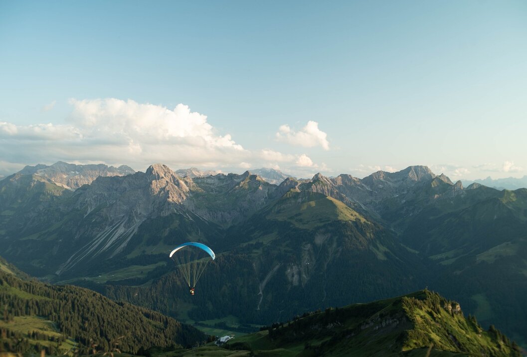Gleitschirmflieger vor Bergpanorama unter blauem Himmel