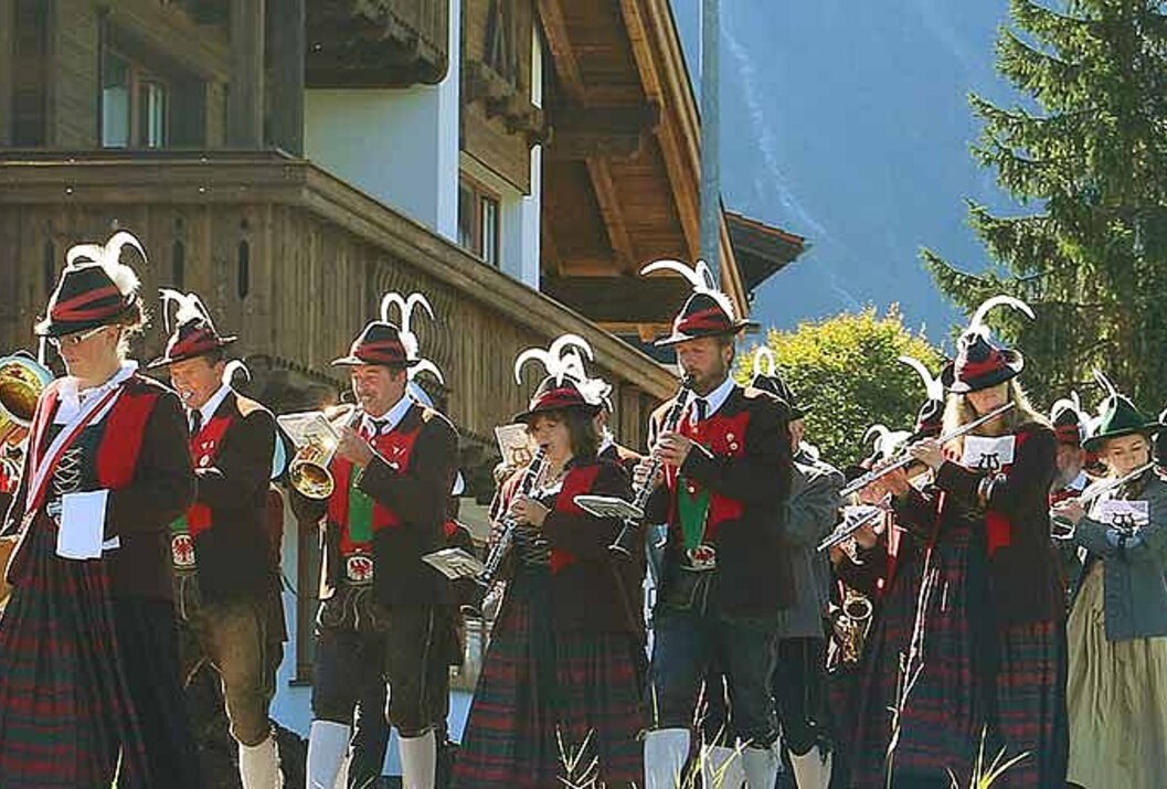 Blasmusikgruppe in Tracht spielt vor einem Holzhaus in den Bergen
