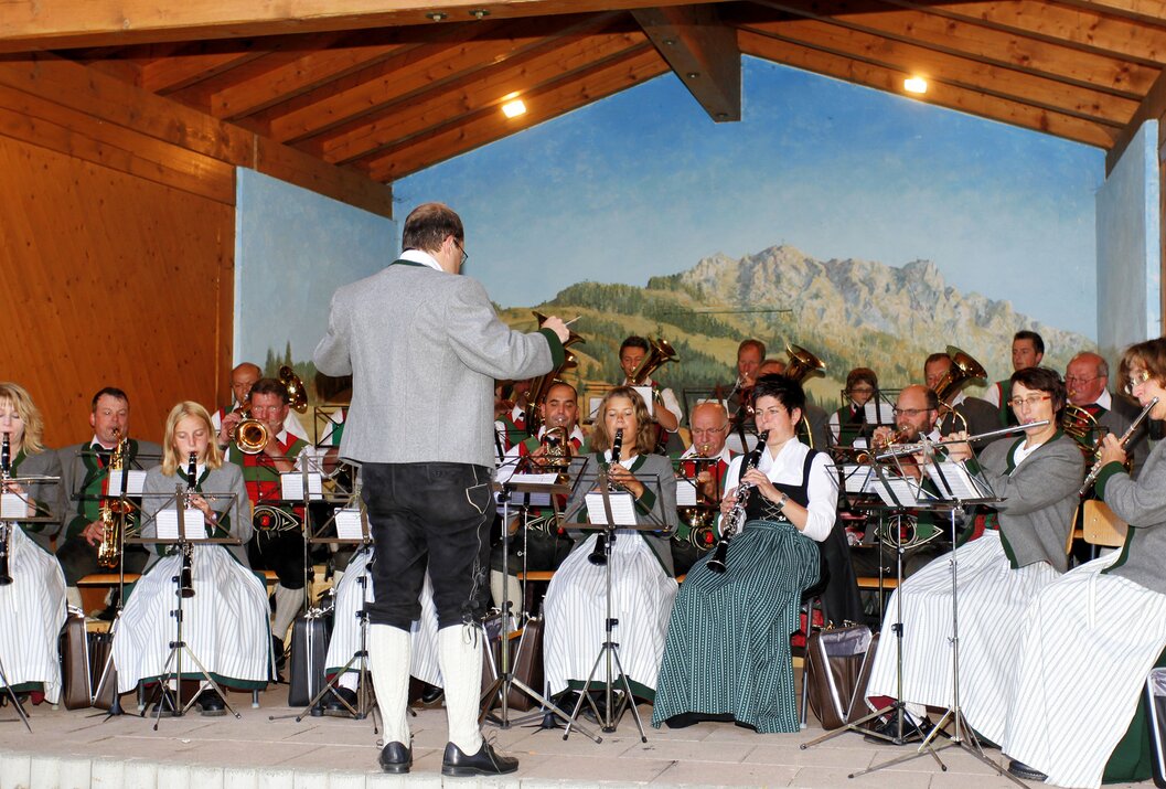 Blasorchester spielt vor Bergkulisse, Dirigent im Vordergrund