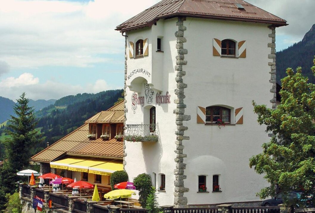 Weißes Gebäude mit Turm, Restaurant mit gelben Sonnenschirmen, grüne Landschaft