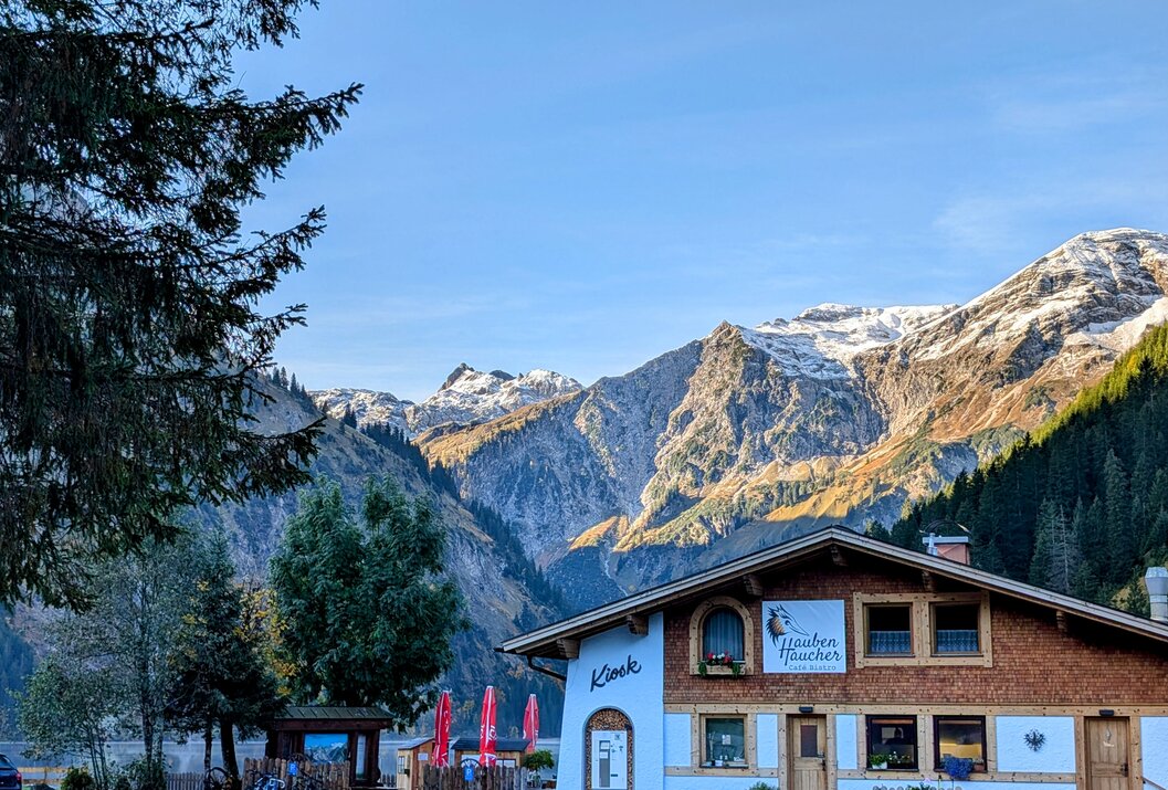 Haus vor Bergkulisse mit Schnee bedeckten Gipfeln unter blauem Himmel