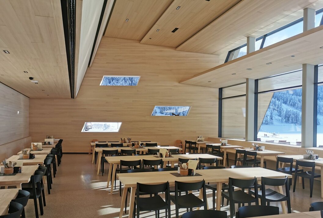 Heller Speisesaal mit Holzwänden, Tischen und Stühlen, Blick durch Fenster auf verschneite Landschaft