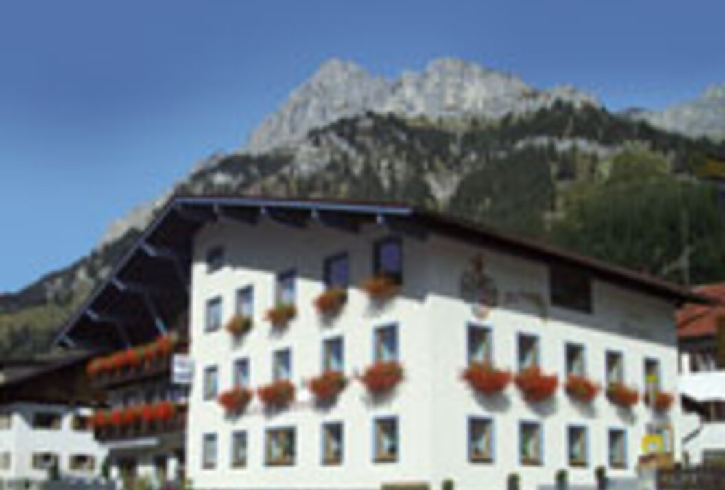 Weißes Gebäude mit roten Blumenkästen vor Bergkulisse