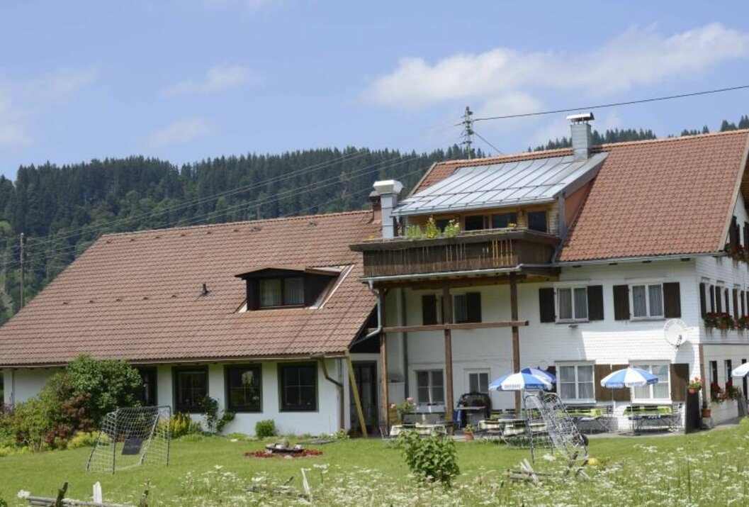 Bauernhaus mit rotem Ziegeldach und Balkon vor bewaldetem Hügel