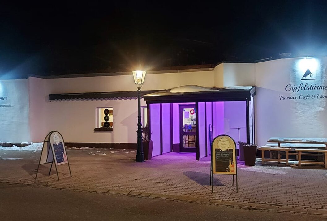 Gebäude mit lila beleuchtetem Eingangsbereich bei Nacht, Laterne und Werbeschilder davor