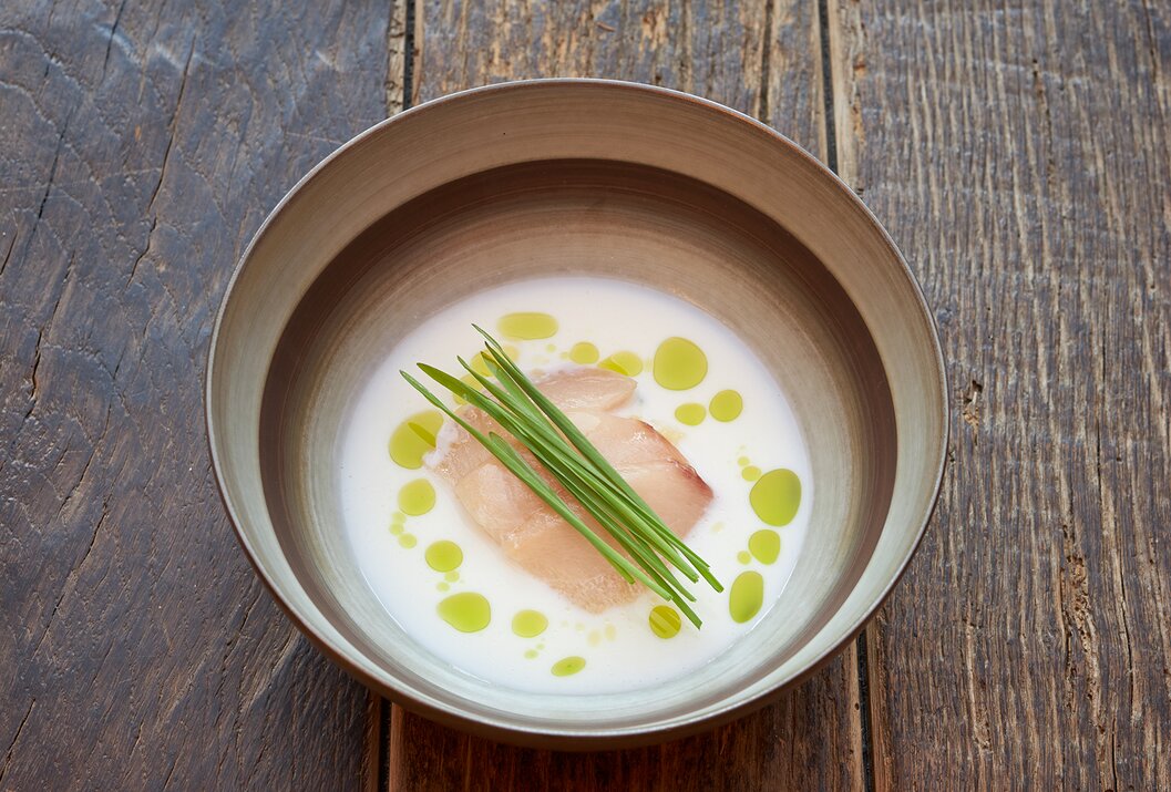 Suppe mit Fisch, Schnittlauch und Öl in einer Schale auf einem Holztisch