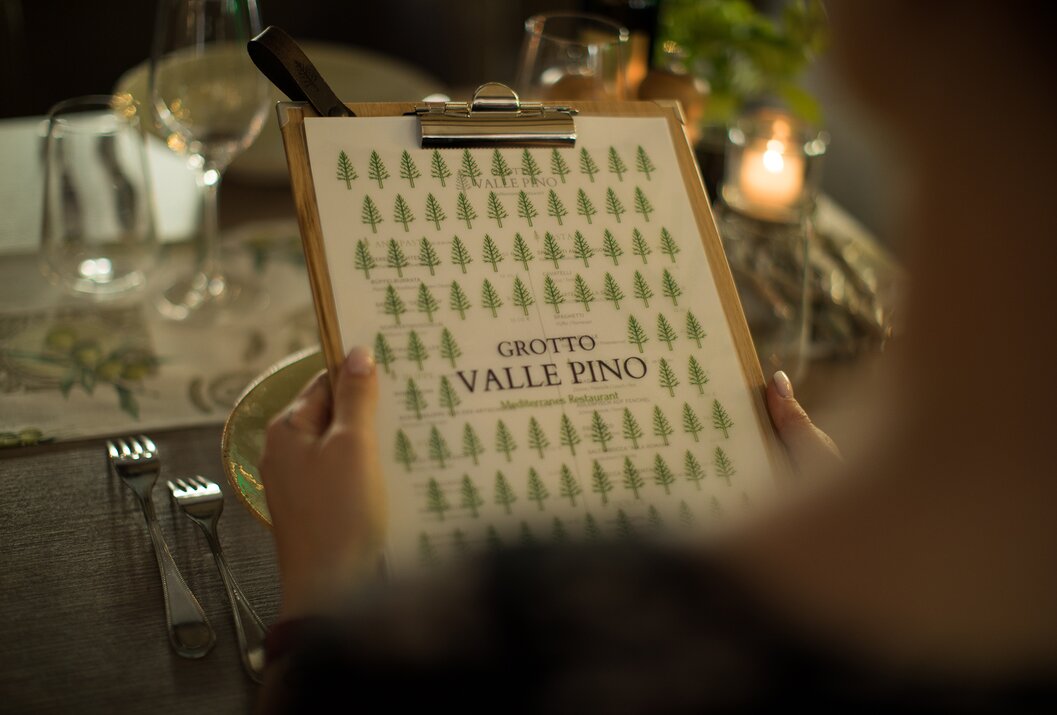 Person hält Speisekarte "Grotto Valle Pino" mit Tannenbaum-Muster