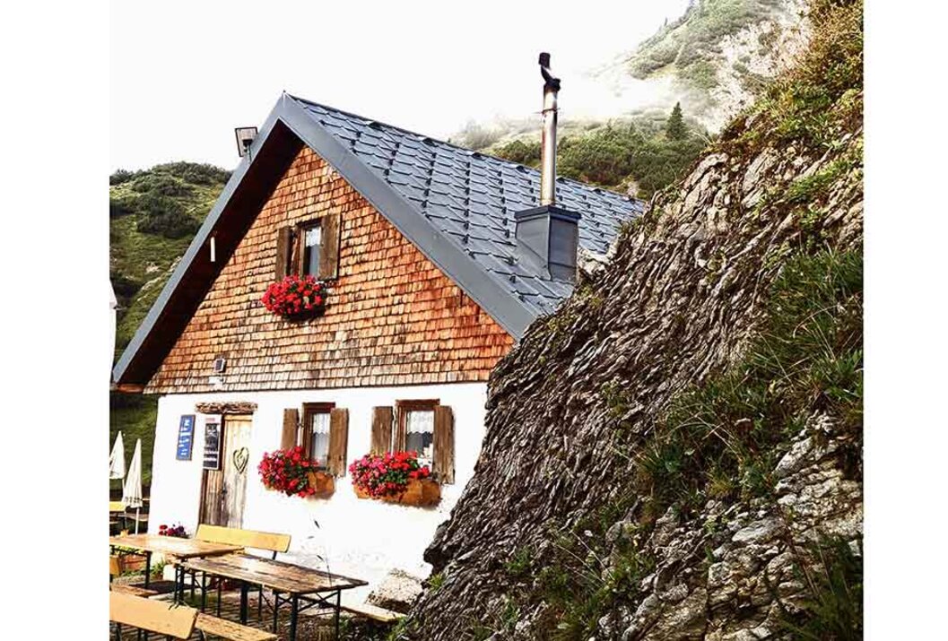 Hütte mit Holzschindeln und roten Blumenkästen neben einem Felsen