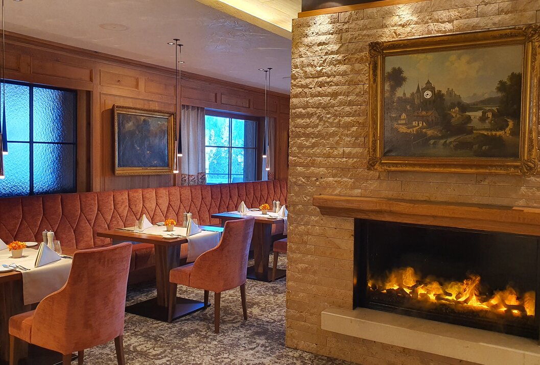 Gemütliches Restaurant mit Kamin, Holzwänden, Kunst und gedeckten Tischen