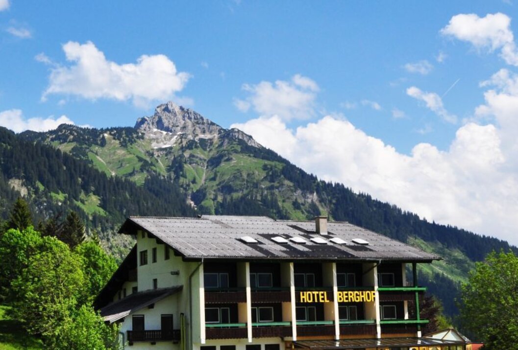 Hotel Berghof vor Bergkulisse mit blauem Himmel und Wolken