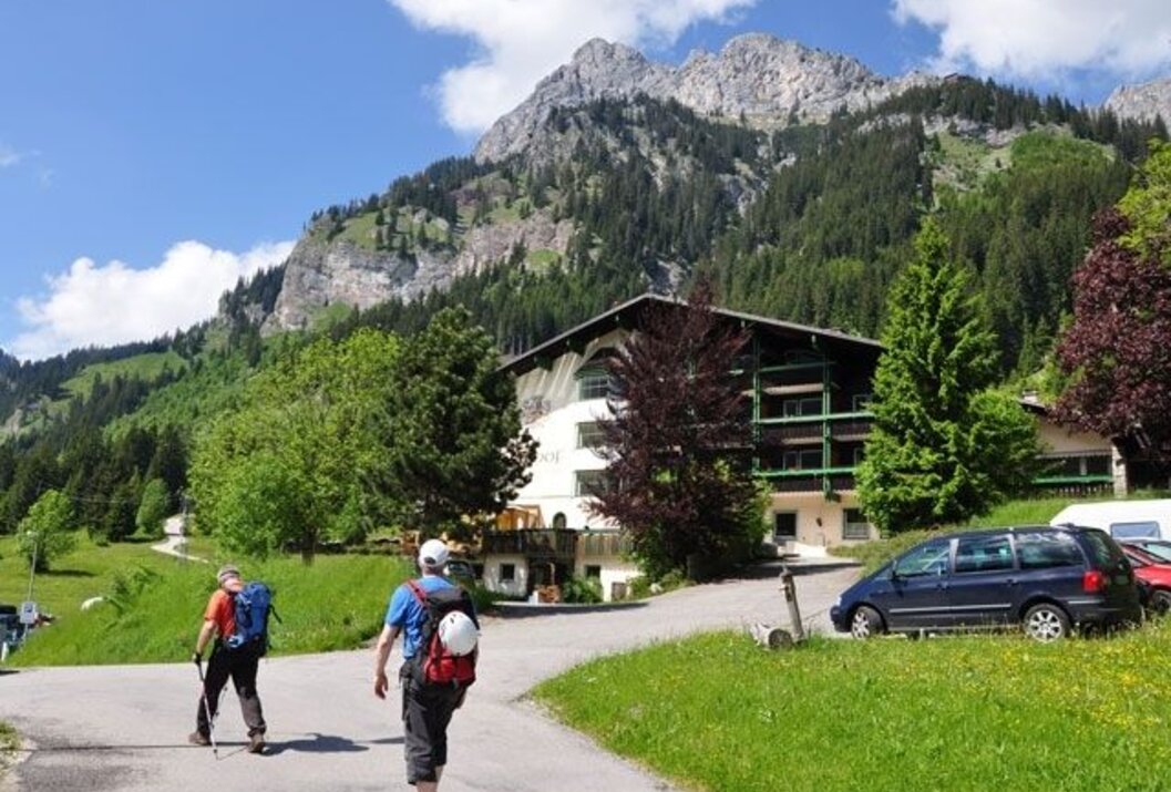 Wanderer auf Straße vor Haus und Berglandschaft