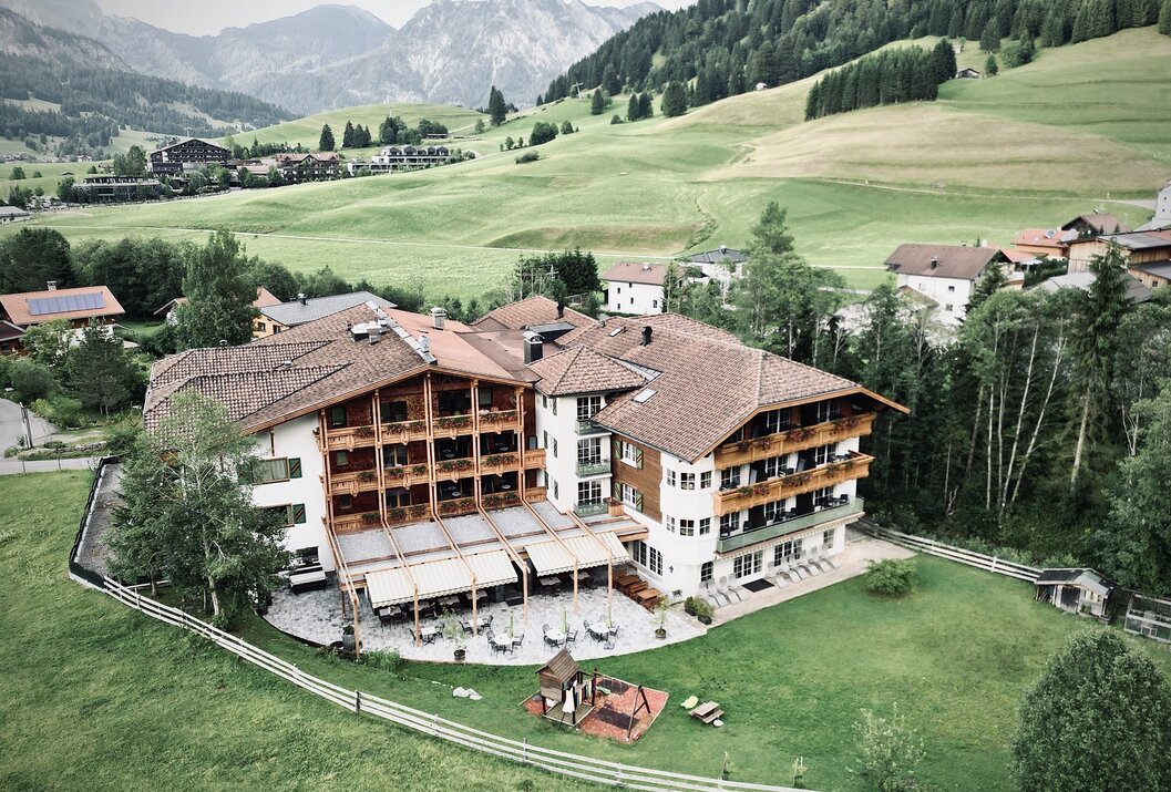 Hotel mit braunem Dach vor grüner Landschaft mit Bergen