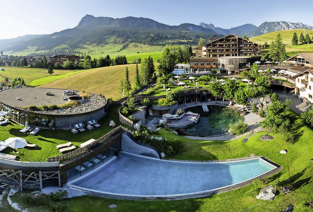 Hotelanlage mit Pool, Garten und Bergen im Hintergrund