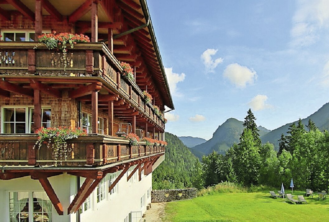 Holzhaus mit Balkonen, Blumenkästen und Blick auf grüne Wiese und Berglandschaft