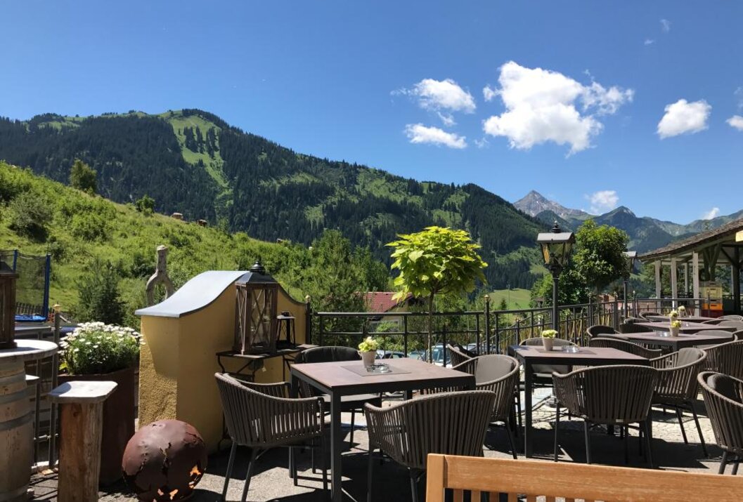Terrasse mit Tischen und Stühlen vor Berglandschaft unter blauem Himmel