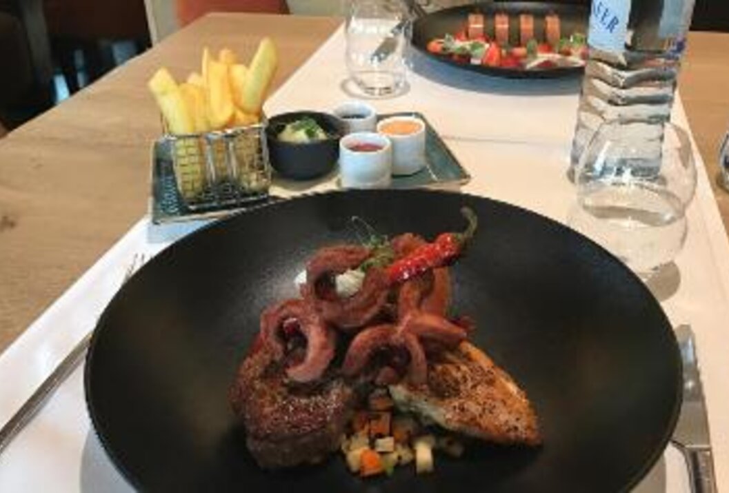 Teller mit Fleisch, Gemüse und Zwiebeln, dazu Pommes, Dips und Erdbeeren auf einem Tisch