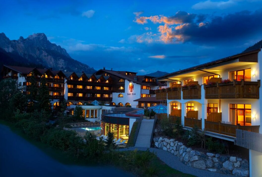 Hotelanlage in den Bergen bei Dämmerung mit beleuchteten Fenstern und Pool