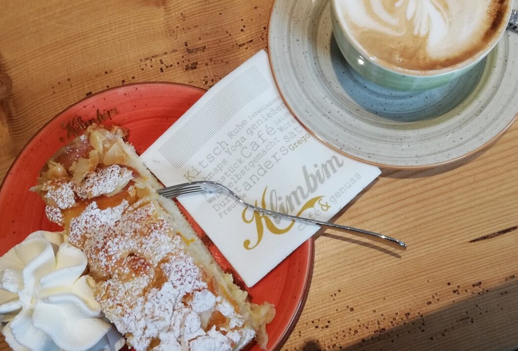 Apfelstrudel mit Puderzucker, Sahne, Gabel, Serviette und Cappuccino auf Holztisch