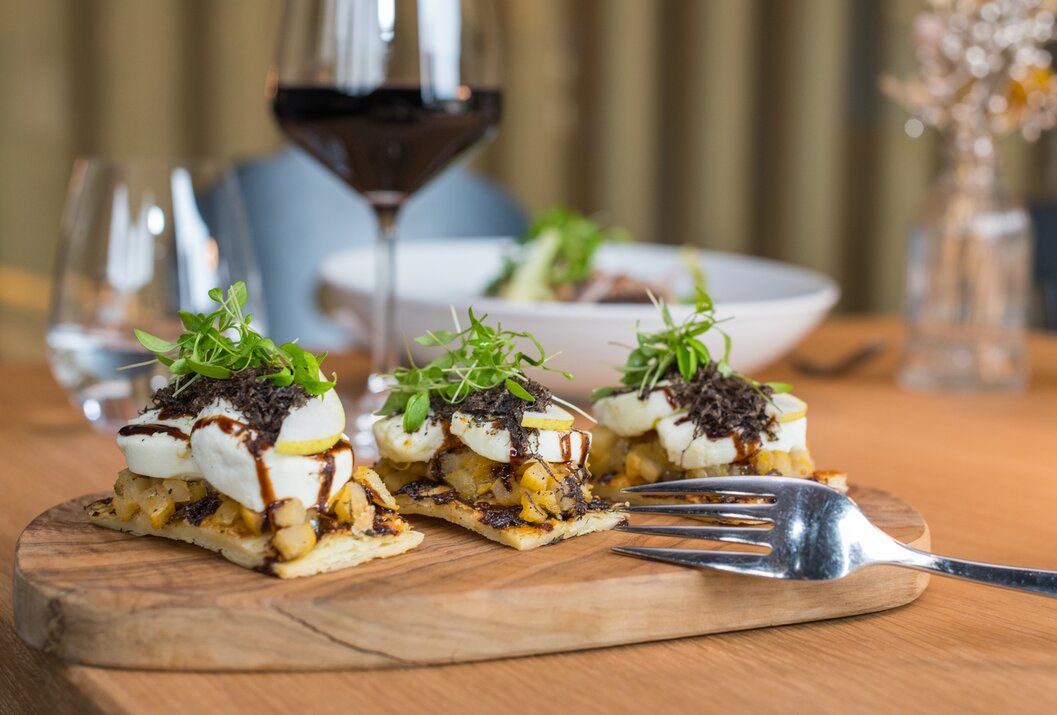 Drei Appetithäppchen auf Holzbrett mit Mozzarella, Trüffel und Salat, dazu ein Glas Rotwein