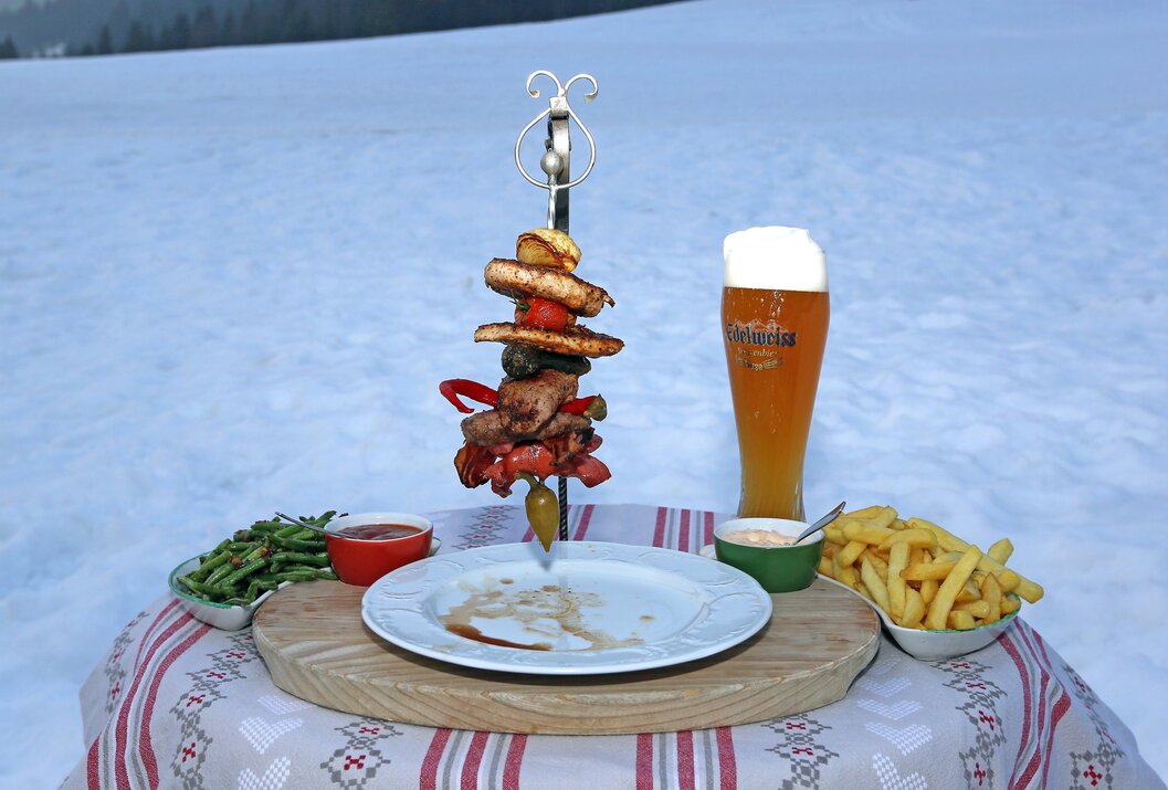 Spieß mit Fleisch und Gemüse, Bier, Pommes, Bohnen und Dips auf einem Tisch im Schnee