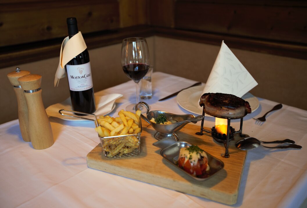 Gedeckter Tisch mit Steak, Pommes, Wein und Soßen auf Holzbrett