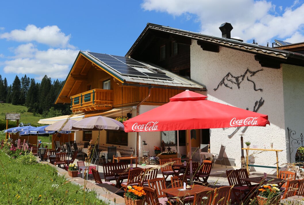 Gasthof mit Terrasse, Sonnenschirmen und Berg-Dekoration an der Fassade