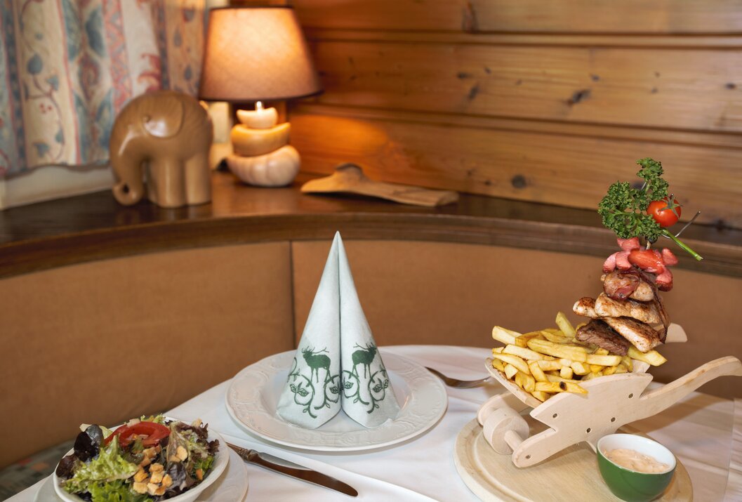 Gedeckter Tisch mit Serviette, Salat, Pommes und Fleisch vor rustikalem Hintergrund