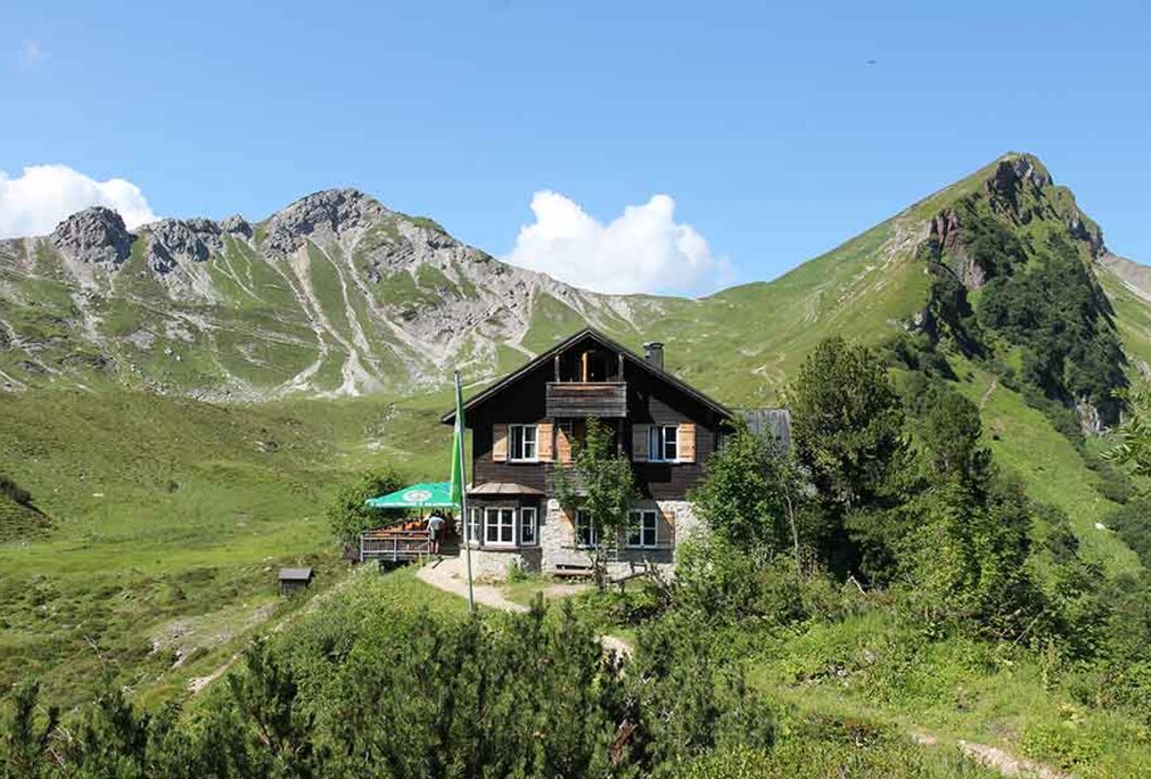 Berghütte vor grünen Hängen und blauem Himmel