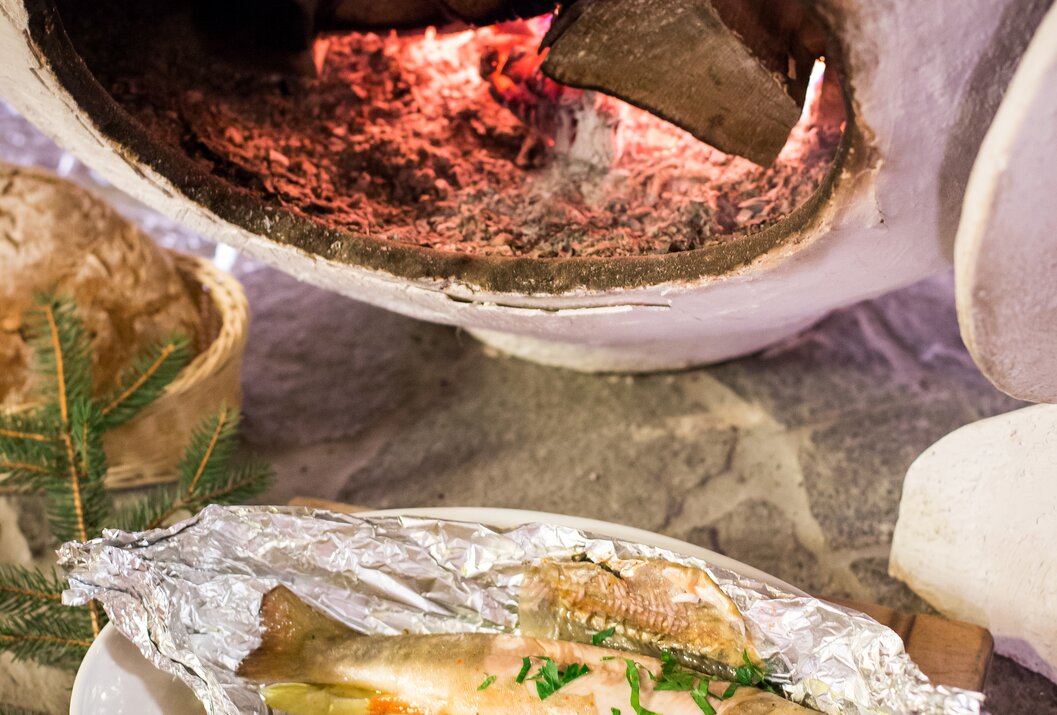 Gebackener Fisch in Alufolie mit Gemüse vor einem Ofen mit brennendem Holz