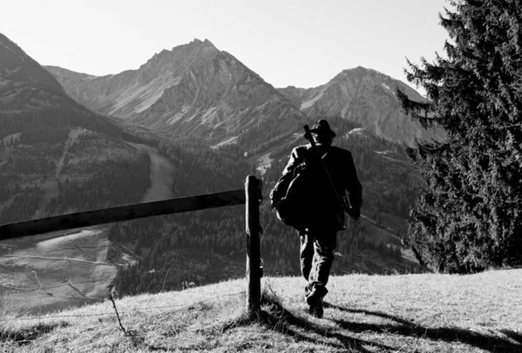 Mann mit Hut und Rucksack wandert in Schwarzweiß vor Bergkulisse
