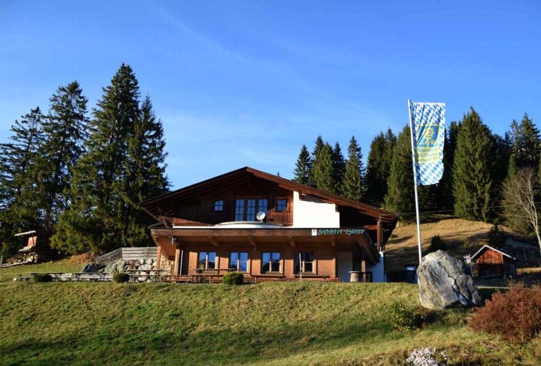 Holzhaus mit bayerischer Flagge auf einem Hügel vor blauem Himmel