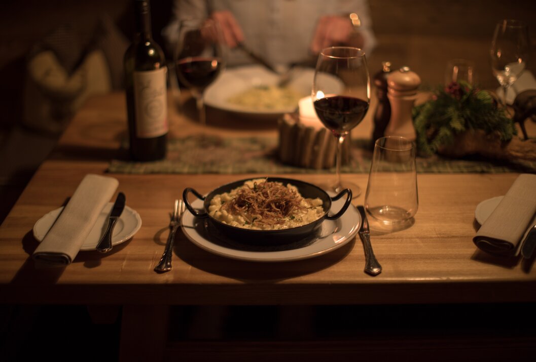 Käsespätzle mit Röstzwiebeln auf gedecktem Tisch mit Wein und Kerze