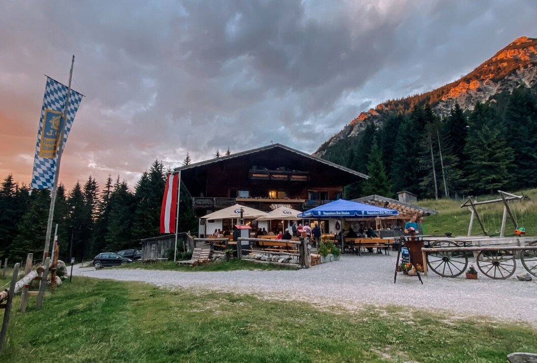 Berghütte mit Biergarten vor Bergkulisse unter bewölktem Himmel