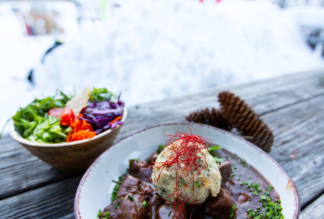 Teller mit Fleischgericht und Knödel, daneben Salat und Tannenzapfen im Schnee