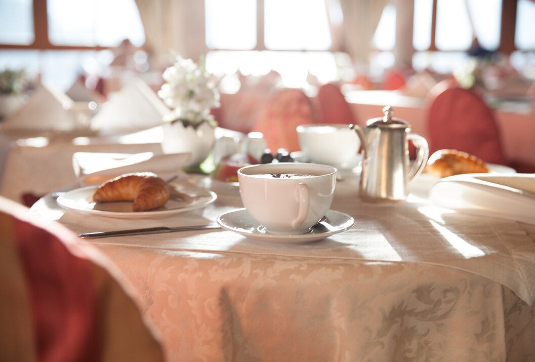 Gedeckter Frühstückstisch mit Croissant, Kaffee, Blumen und Kanne im hellen Raum