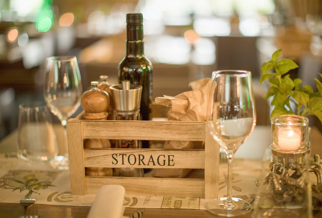 Gedeckter Tisch mit Holzkiste, Ölflasche, Gewürzen und Weingläsern