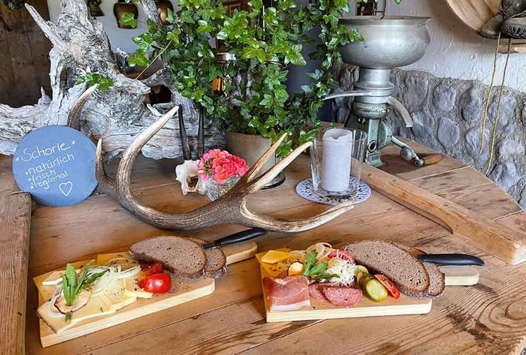 Rustikaler Tisch mit Brotzeit, Geweih, Pflanze und alter Milchzentrifuge